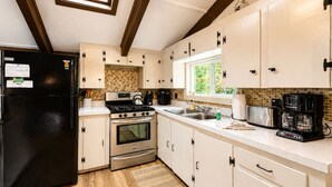 A kitchen with a black refrigerator, stainless steel stove, and oven, white cabinets, a window with a view, and a tiled backsplash. - Bartlett Cabin 4 Min to Storyland / Fire Pit/ Dog friendly / Near Attitash (Bartlett)