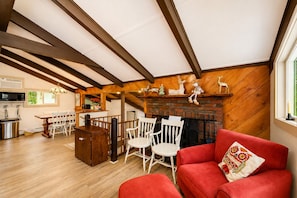 Ein gemütliches Wohnzimmer mit Kamin, Holzbalken, einem roten Sofa und einem Essbereich mit Stühlen und einem Tisch.