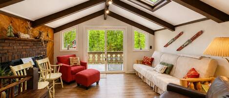 A spacious loft with a high ceiling, wooden beams, a fireplace, and a large sliding glass door leading to a balcony.