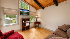 A room with a wooden ceiling, a television mounted on the wall, a wooden cabinet with a window view, a desk with a lamp, and a red sofa. - Bartlett Cabin 4 Min to Storyland / Fire Pit/ Dog friendly / Near Attitash (Bartlett)