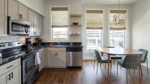 Una cocina moderna con horno, microondas y lavavajillas de acero inoxidable, armarios de madera y un comedor con mesa redonda y sillas.