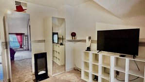 Un salon avec un téléviseur posé sur un meuble, une bibliothèque et une porte donnant sur une autre pièce.