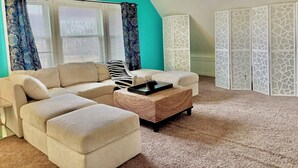 Un salon avec un mur d’accent de couleur turquoise, un ventilateur de plafond, un canapé d’angle, une table basse et un paravent décoratif.