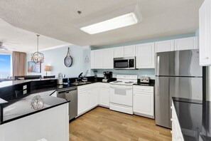 Una cocina moderna con armarios blancos, microondas, estufa, refrigerador y comedor con encimera negra.
