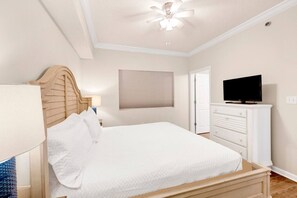 Ein Schlafzimmer mit einem Bett, einem Fernseher auf einer Kommode, einem Deckenventilator und einem Fenster mit Jalousien.