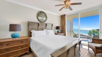 A bedroom with a bed, a nightstand, a lamp, a ceiling fan, and a view of the ocean.