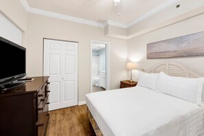 Habitación de hotel con cama, televisor, cómoda y baño visible a través de una puerta abierta.