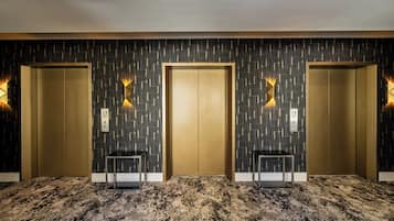 A hotel lobby with three elevators, a patterned wall, and a carpeted floor.
