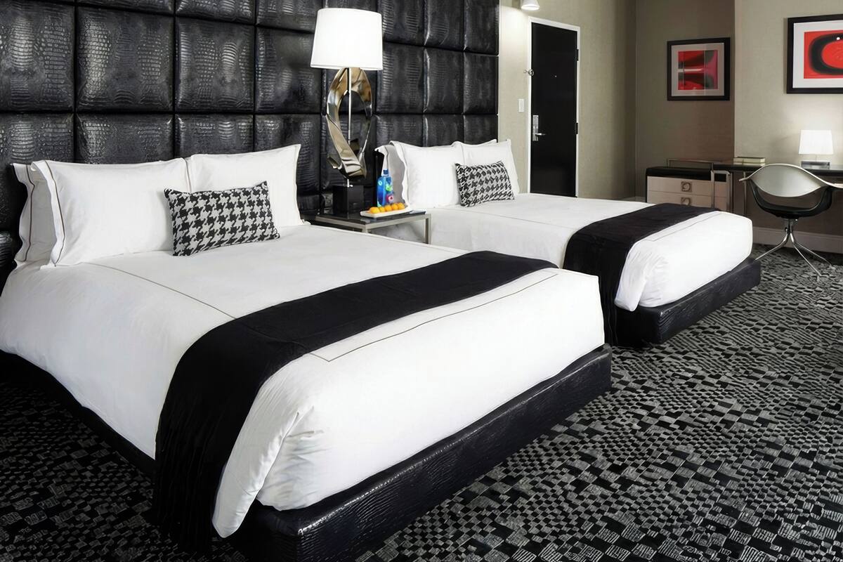 A hotel room with two beds, a black headboard, a patterned carpet, and a desk with a chair.