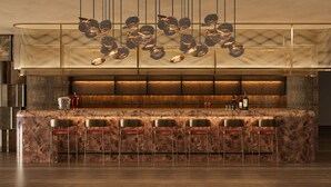 Eine Bar mit einer Marmorplatte, Barhocker, einer hängenden Leuchte und einer Weinflasche auf der Theke.