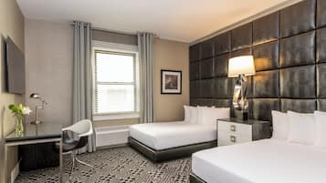 Habitación de hotel con cama, mesita de noche, lámpara, escritorio, silla y ventana con cortinas.