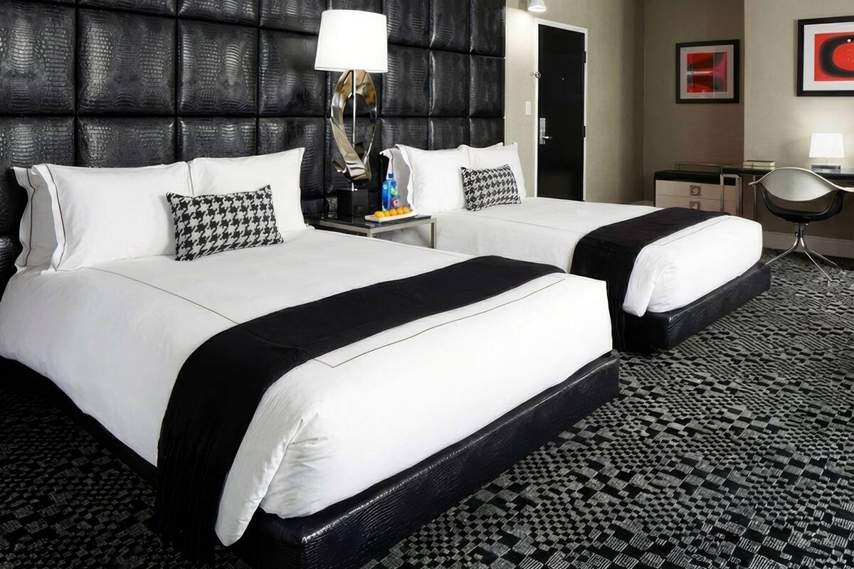 A hotel room with two beds, a black headboard, a patterned carpet, a desk, and a chair.
