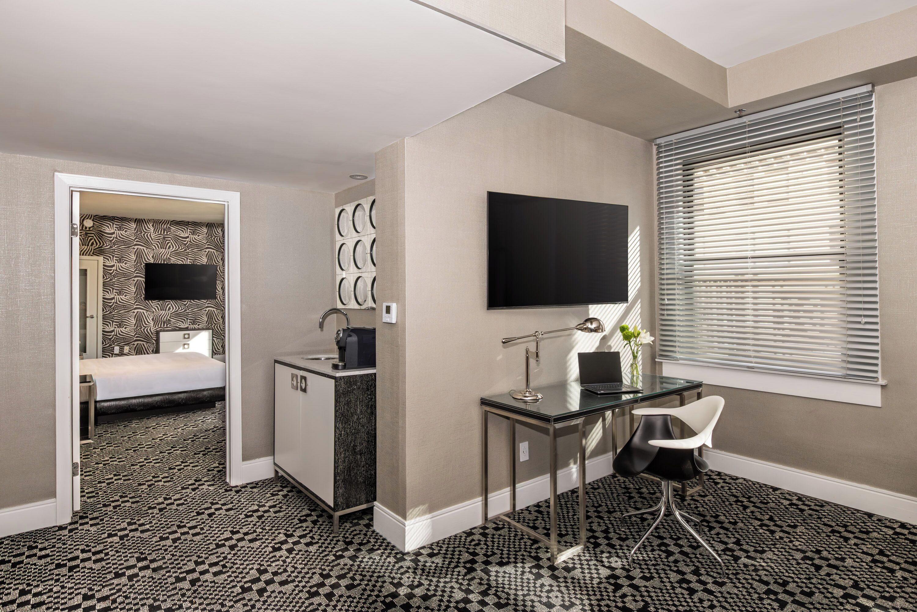 A hotel room with a bed, a desk, a TV, and a window with blinds.