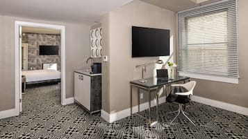 A hotel room with a bed, a desk, a TV, and a window with blinds.