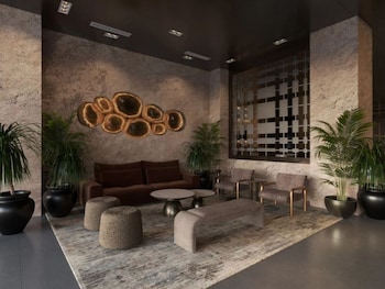A hotel room with a zebra-patterned wall, a large mirror, a bed with white linens, a bedside table with a lamp, and a black storage bench. at Hotel Clark