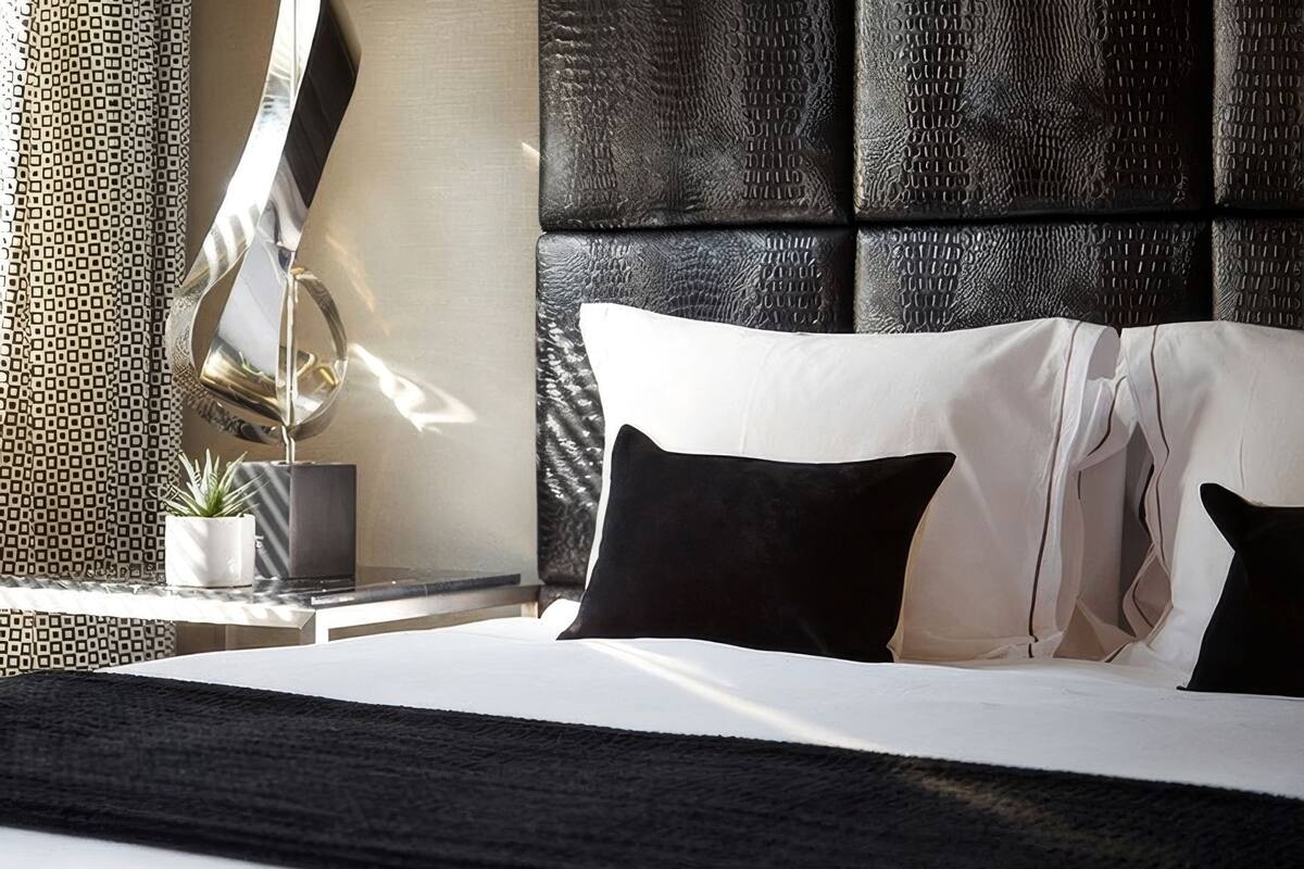 A modern hotel room with a large bed, a potted plant, and a textured headboard.