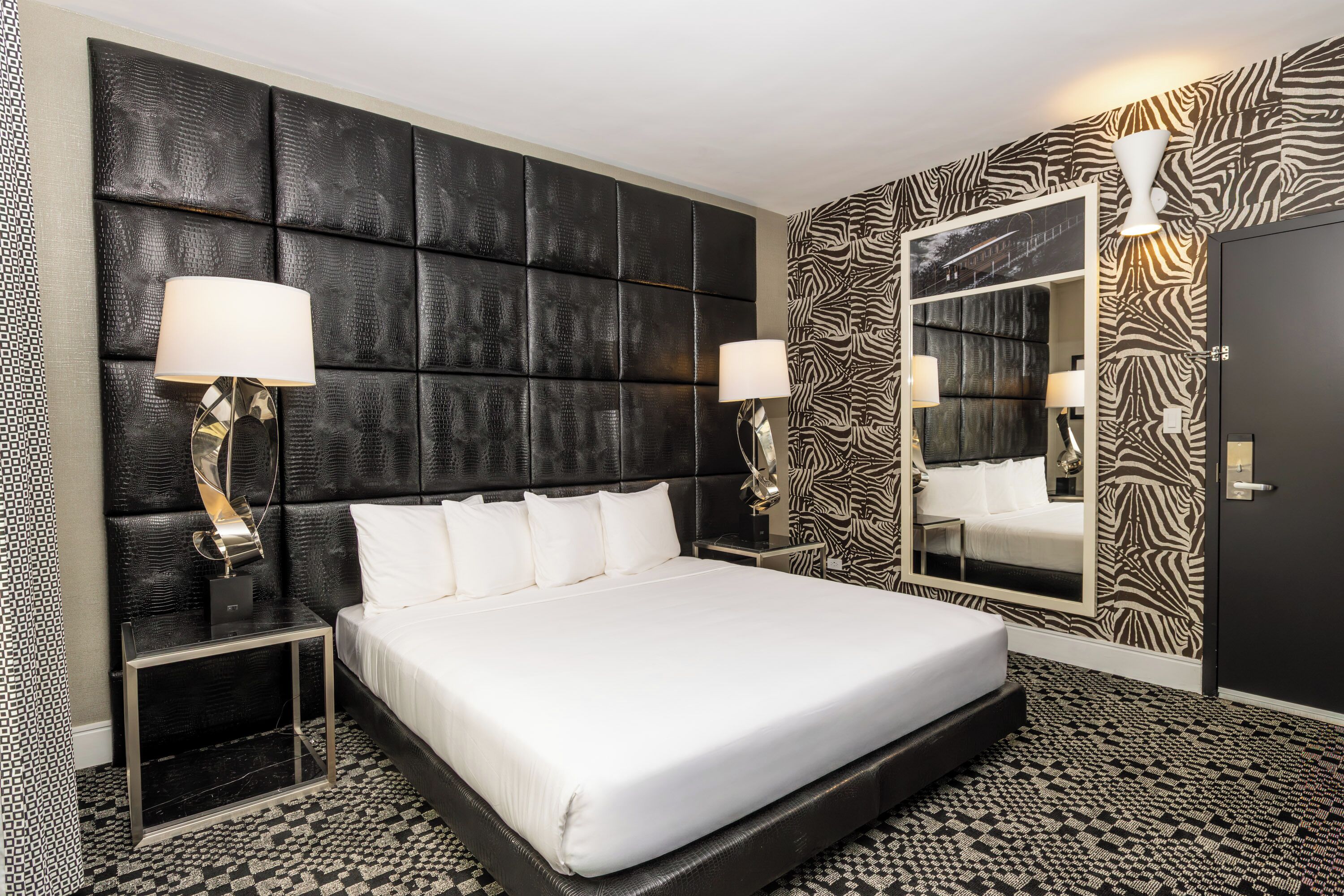 A hotel room with a large bed, two bedside lamps, a zebra-patterned wall, and a large mirror.
