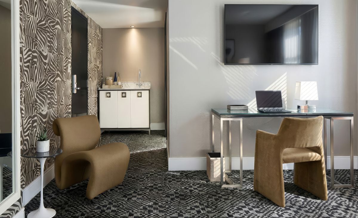 A hotel room with a sofa, a desk with a laptop, a TV, and a minibar.