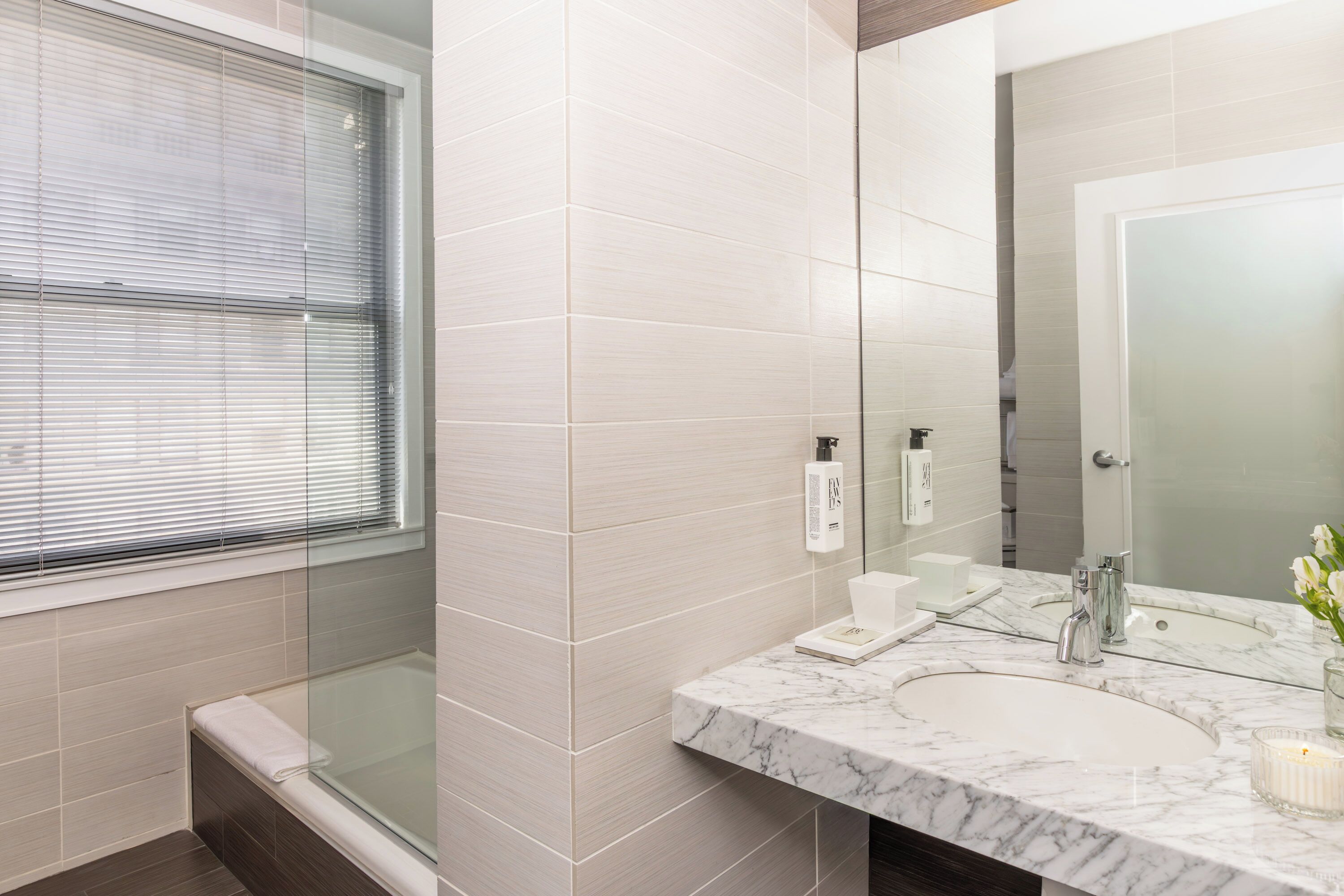 A modern bathroom with a glass shower enclosure, a marble sink, and a large mirror.