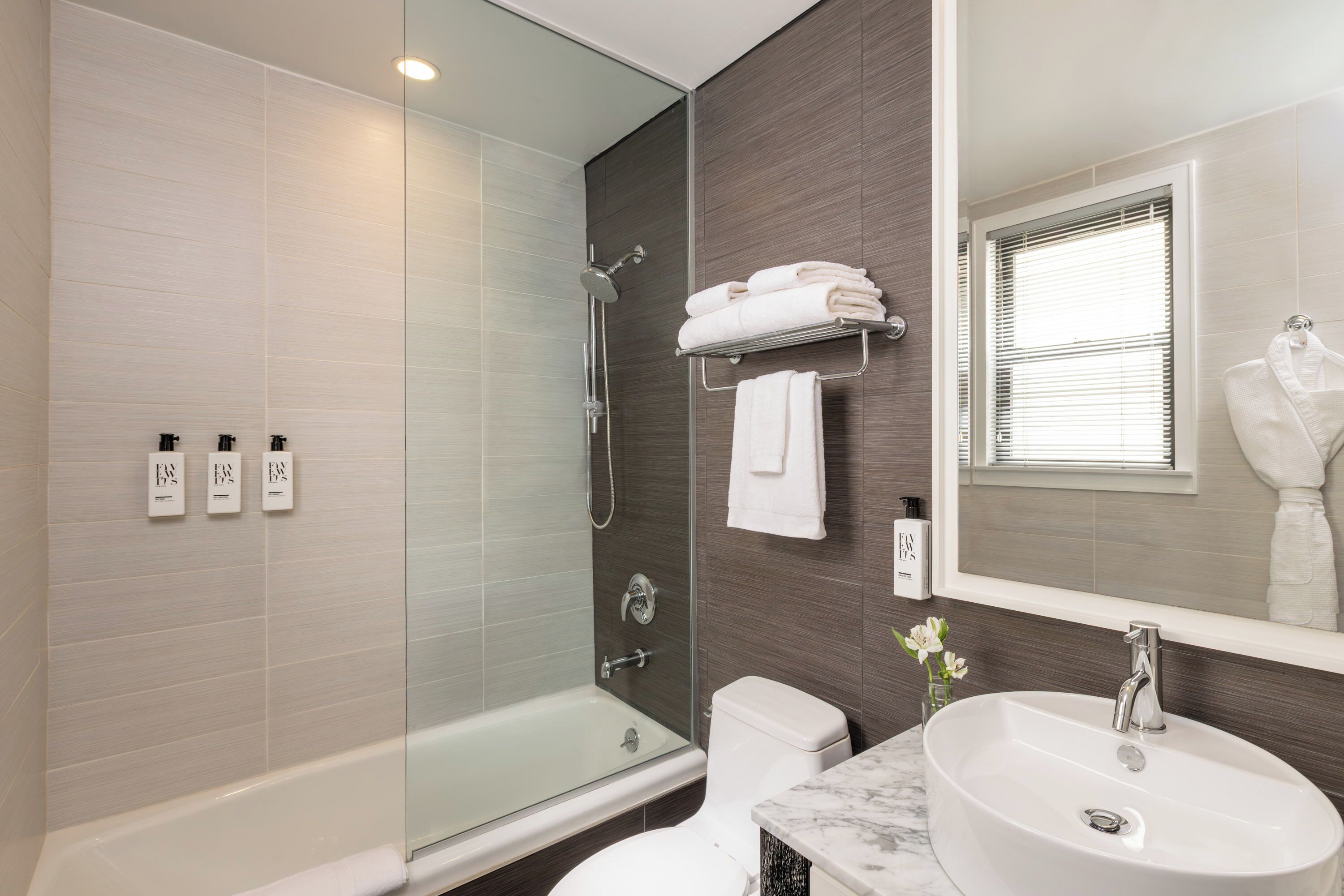 Un baño moderno con ducha envuelta en vidrio, inodoro blanco, lavabo de mármol y un espejo grande.