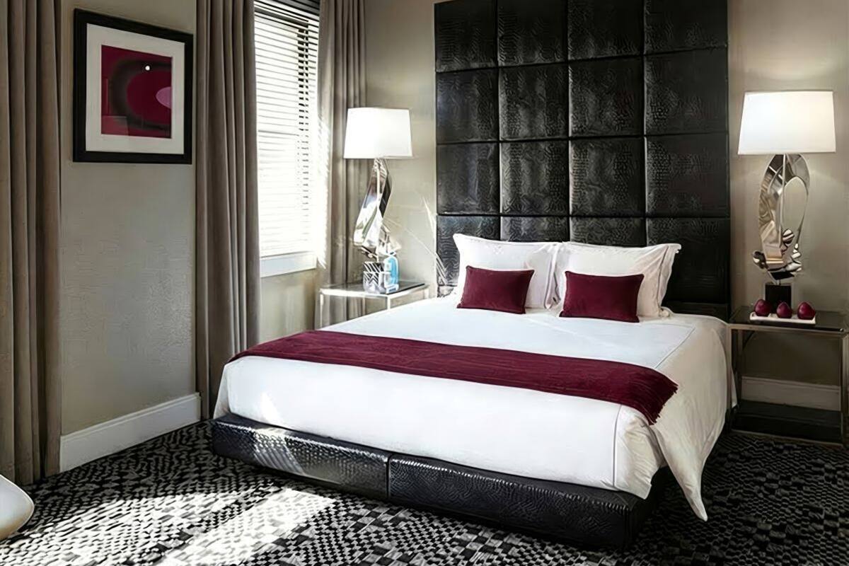 A hotel room with a large bed, a headboard, two bedside tables with lamps, a framed picture on the wall, and a patterned rug.