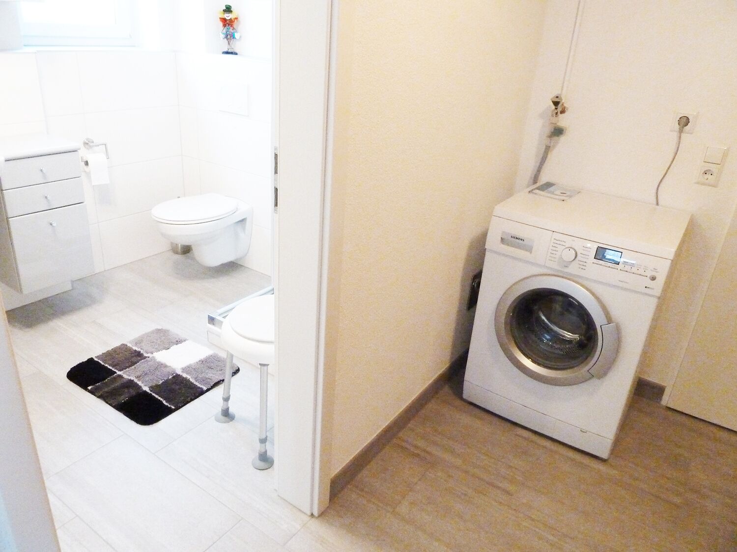 Ein kleiner Hauswirtschaftsraum mit einer Waschmaschine mit Frontlader, einer Toilette und einem Teppich.