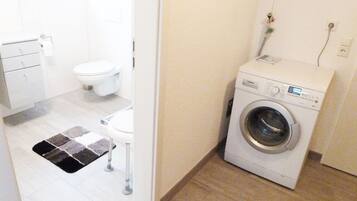 Ein kleiner Hauswirtschaftsraum mit einer Waschmaschine mit Frontlader, einer Toilette und einem Teppich.