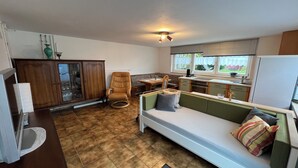 Un espace de vie compact comprenant un coin cuisine, un coin repas et un espace détente avec un canapé et un fauteuil.