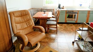 Une cuisine chaleureuse avec un coin repas, comprenant un fauteuil en cuir marron, une table à manger avec des chaises et un comptoir de cuisine équipé d’appareils électroménagers.