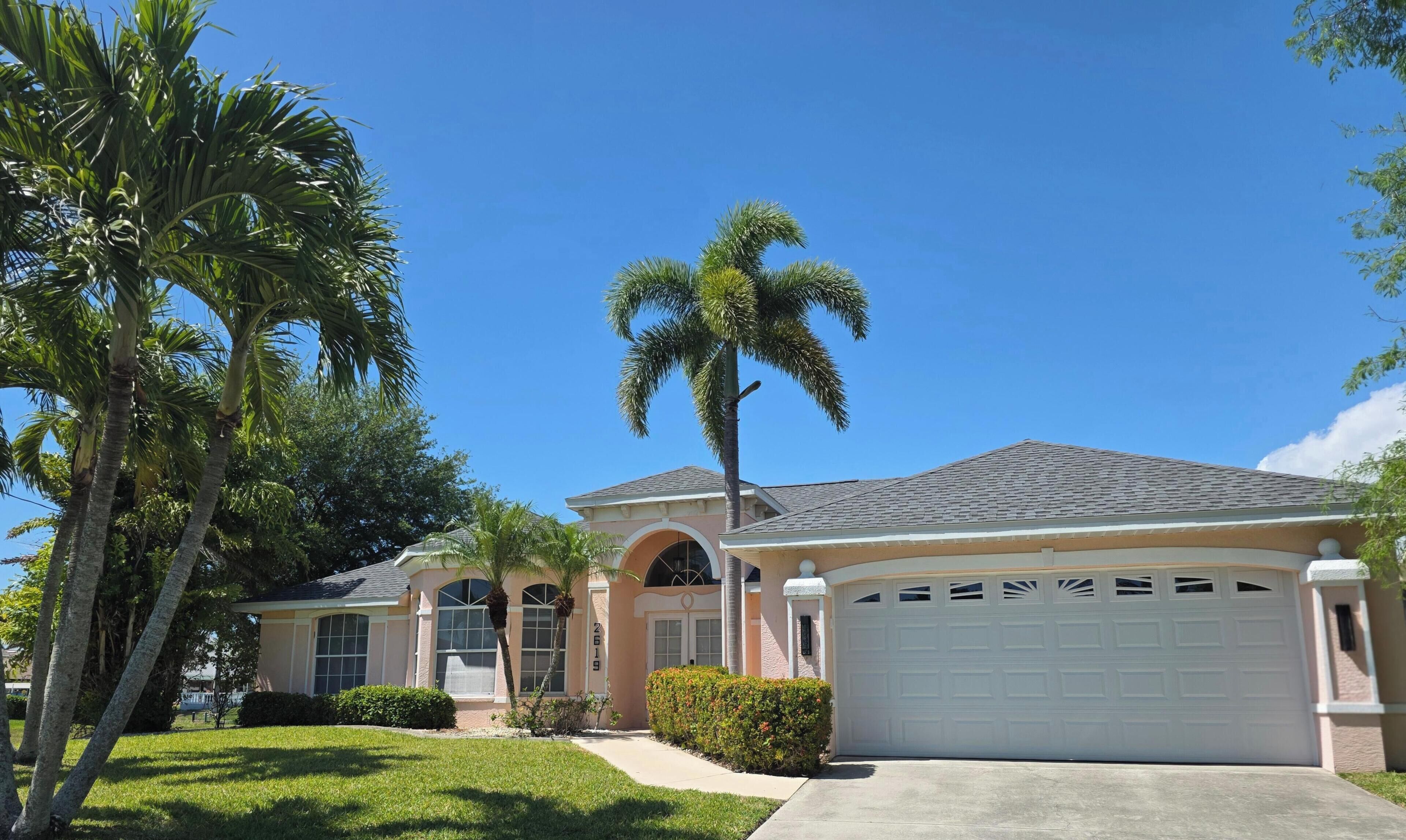 A residential house with a garage, palm trees, and a clear blue sky.
