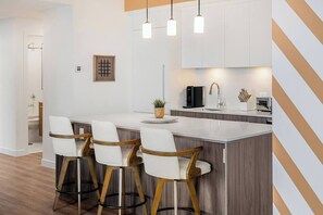 Een moderne keuken met een centraal eiland, barstoelen, hanglampen en een koffieapparaat.