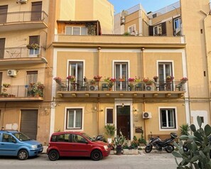 Un immeuble à plusieurs étages doté de balcons, une voiture rouge garée devant et une moto garée sur le côté.