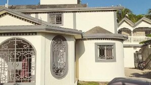 Un edificio de fachada simétrica, con un ventanal central en arco y ornamentación metálica detallada, una ventana más pequeña con diseño parecido, y un techo plano con chimenea.