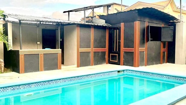 Una piscina con borde de azulejos y un área techada con listones de madera verticales.