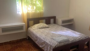 Un dormitorio con una cama, un ventanal con cortinas, un estante blanco y baldosas de suelo estampadas.