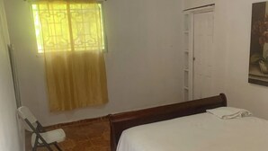 Un dormitorio con cama, una silla, un ventanal con cortina y una puerta.
