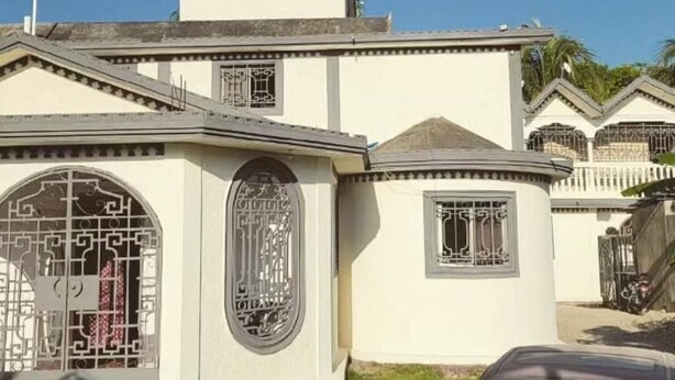 Un bâtiment à la façade symétrique, orné d'une fenêtre centrale en arc surmontée de motifs métalliques complexes, d'une fenêtre plus petite au design similaire et d'un toit plat avec une cheminée.
