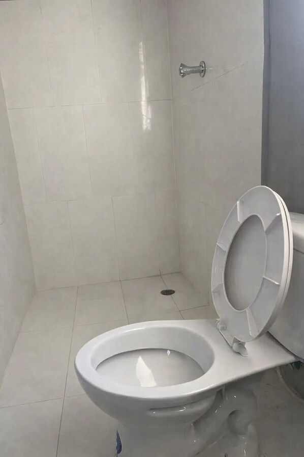 Un baño moderno con inodoro blanco, zona de ducha y desagüe visible.