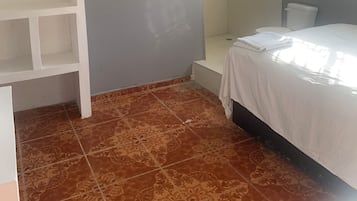 A bedroom with a bed, a white wardrobe, a shower, and a window.