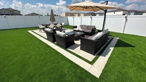 Une terrasse à l’arrière de la maison, avec des meubles d’extérieur, une table et un grand parasol.