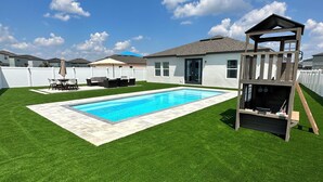 Un jardin avec une piscine, une cabane en bois et une clôture blanche.