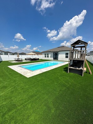 A backyard with a swimming pool, a wooden playhouse, and a white fence. - Disney World 15min! Private Pool 4 Bedroom Themed House! (Davenport)