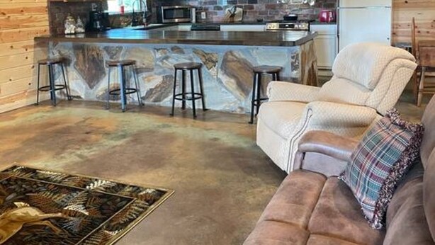 Un vaste espace de vie comprenant un grand canapé, une table basse et une cuisine dotée de meubles en bois et d’un pare-feu en pierre.