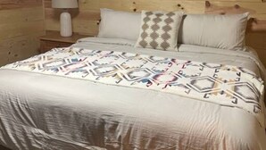 Un lit recouvert d’une couvre-lit à motifs, avec deux oreillers et une lampe de chevet, dans une pièce aux murs en bois.