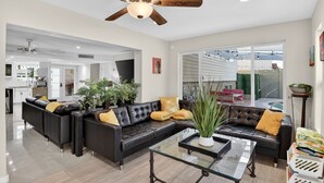 A spacious living room with a black leather sofa, a glass coffee table, and a ceiling fan. - Two Homes w/ Pool, 8BR Mesa Retreat, Sleeps 24 (Mesa)