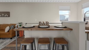 Una zona de cocina con encimera de madera, tres taburetes, un cartel de bar y un sofá al fondo.