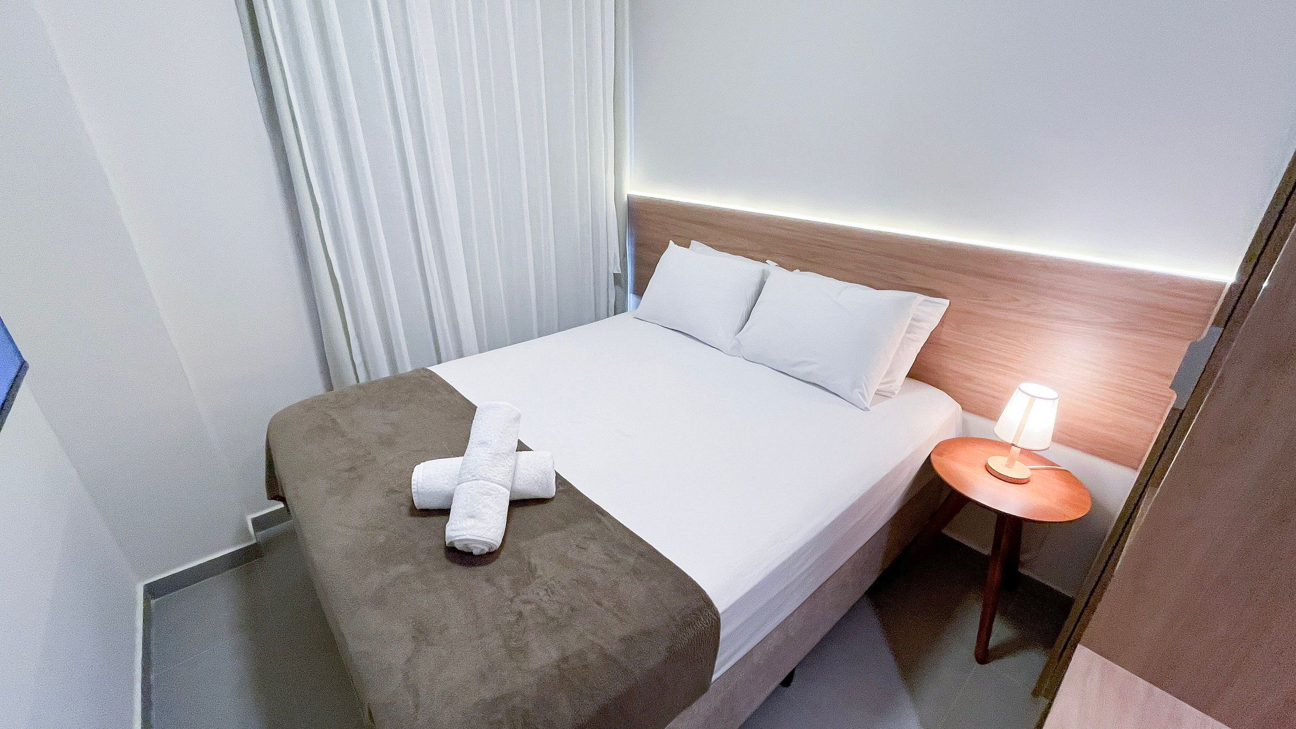 Ein Hotelzimmer mit einem Bett, einem Nachttisch mit Lampe und einem Fenster mit Vorhängen.