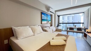A hotel room with a large bed, a balcony with a table and chairs, and a painting on the wall. - Studios Nomar Ecoliving - Carneiros (Tamandaré)