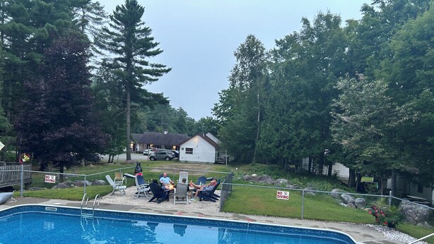 A swimming pool with a 'No Diving' sign, surrounded by trees and a fenced area with chairs.