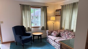 A room with a blue armchair, a floral sofa, a small round table, and a floor lamp.